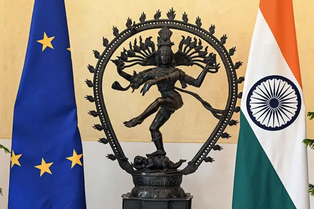 Las banderas de la UE e India flanqueando una pequeña escultura. 