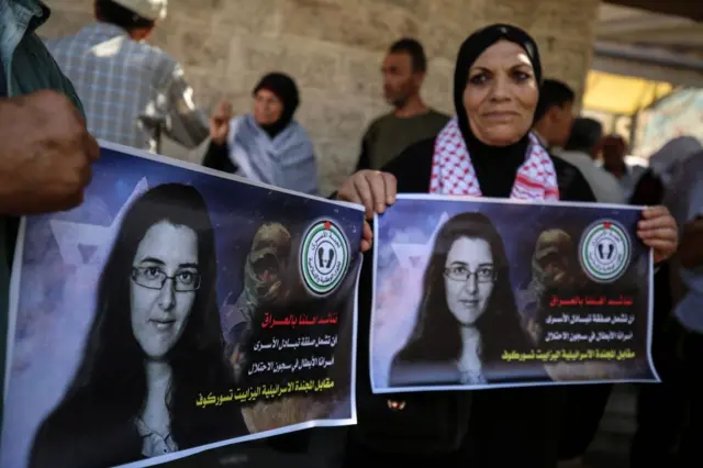 Женщина в хиджабе и с арафаткой на шее и еще один человек, не вошедший в кадр, держат в руках плакаты с портретом Цурковой