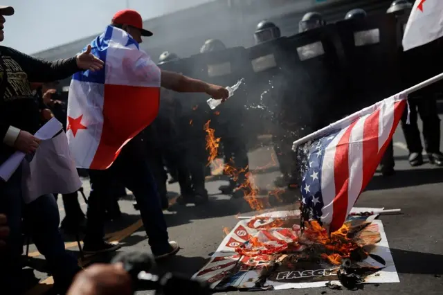 Un hombre con la bandera de Panamá en la espalda le echa agua a una bandera de EE.UU. en llamas