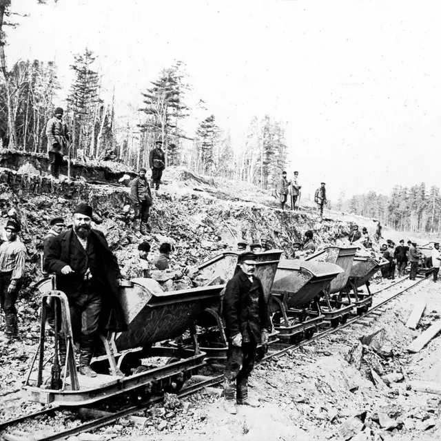 Fotografía en blanco y negro mostrando prisioneros y guardias en un ferrocarril en un campo abierto en Rusia.