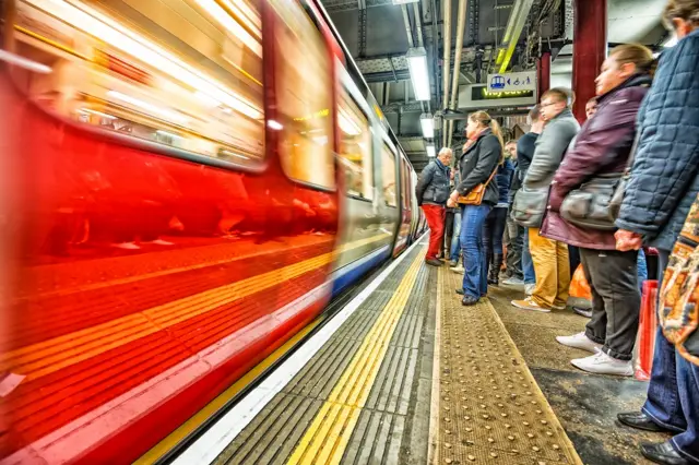 As pessoas esperam o metrô atrás da linha amarela