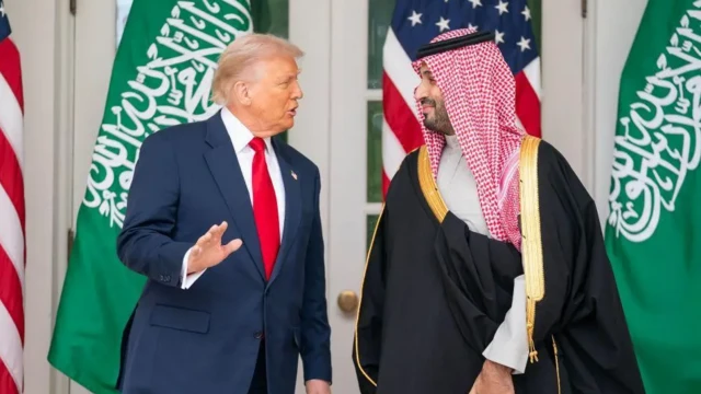 دونالد ترامپ و محمد بن سلمان در کنار هم ایستاده و در حال گفتوگو هستند، پرچمهای دو کشور آمریکا و عربستان سعودی در پشت سر آنها