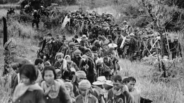 Grupo de refugiados caminhando por matagal em foto em preto e branco