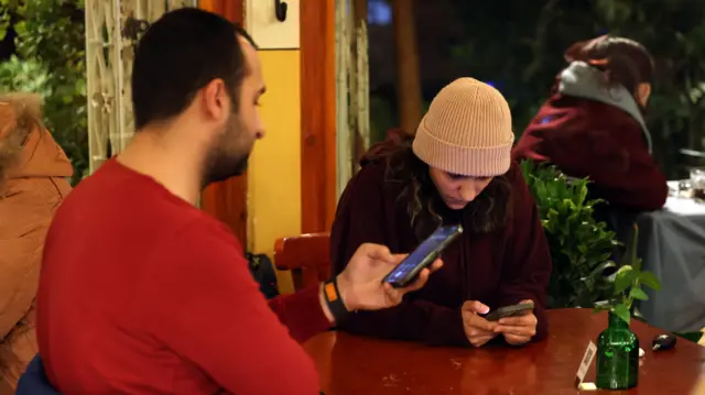 muškarac i žena gledaju u telefone dok sede u kafiću