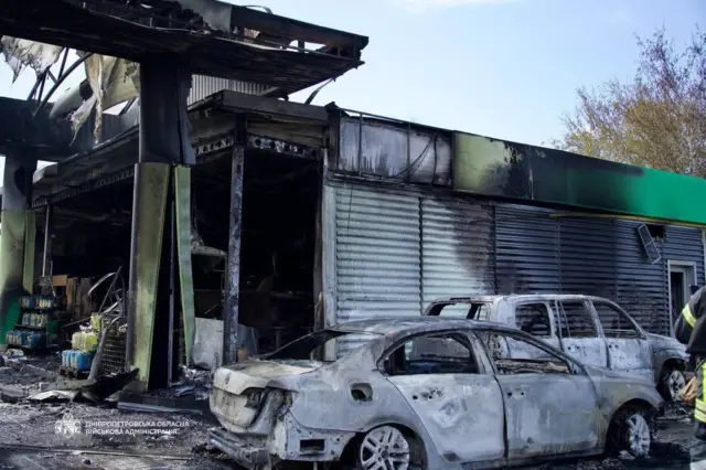 Две сгоревшие машины около одноэтажного здания автозаправки, по которому ударил дрон.