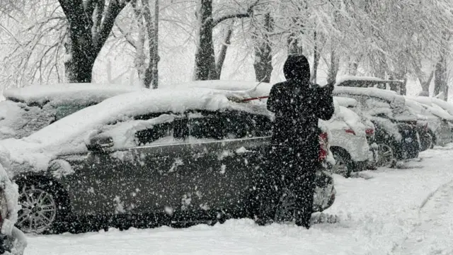 Čovek stoji pored automobila dok pada sneg u Sarajevu