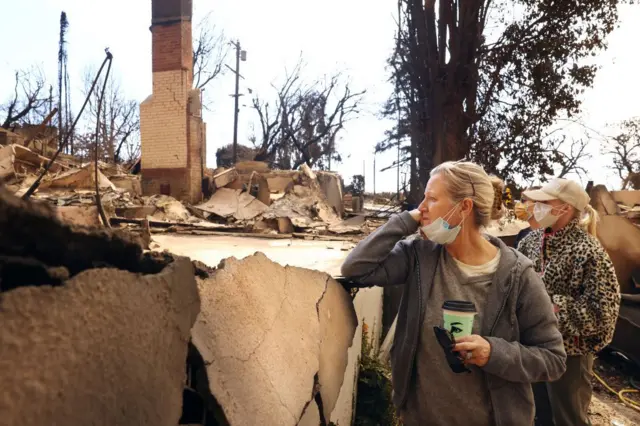 Ana Ashby, delante, y sus hijas Antonia (izquierda), de 23 años, y Judi, de 25, observan la vivienda destruida de sus vecinos en Pacific Palisades, condado de Los Ángeles, California, el 11 de enero de 2025.