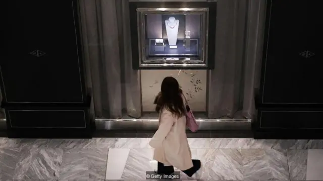 Seorang perempuan memerhatikan perhiasan di dalam etalase toko