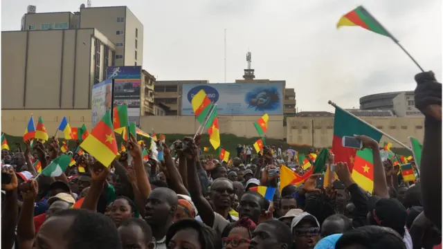 People dey street with Cameroon flag.