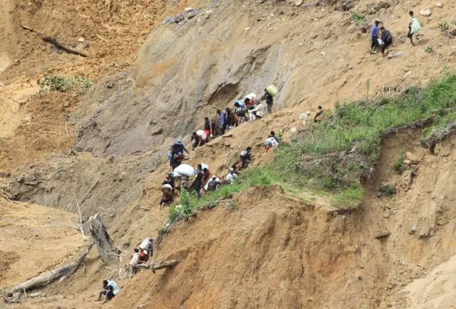Foto udara sejumlah warga memanggul barang saat melintasi jalan yang tertimbun tanah longsor di Desa Burni Pase, Kecamatan Permata, Bener Meriah, Aceh, Sabtu (13/12/2025).