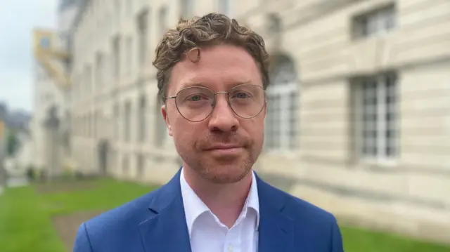 Jonathan Pryor, a bearded man in a blue jacket and white shirt wearing glasses, standing outside Leeds Civic Hall.