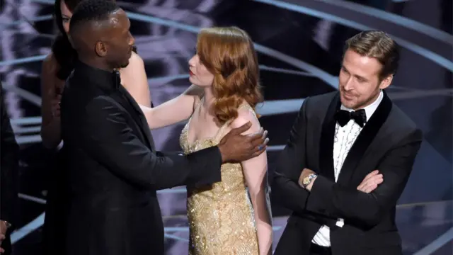 Mahershala Ali de Moonlight abraza a Emma Stone, que ganó el premio a la mejor actriz por La La Land, mientras su coestrella Ryan Gosling mira, confundido.
