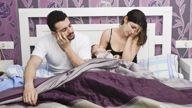 Padres en una cama con el bebé en medio.