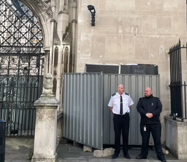 Dvojica članova obezbeđenja stoje ispred metalnih barijera iza kojih je Benksijev mural 