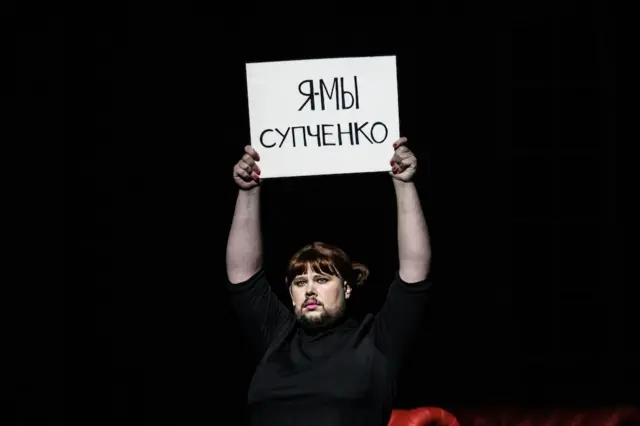 Фрагмент спектакля «На всякого мудреца довольно простоты» — актер держит плакат «Я/Мы Супченко»