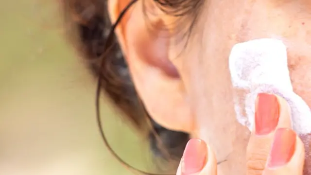 Mujer aplicando crema en una mejilla.