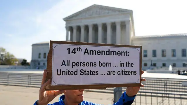 ایک شخص نے بینر اٹھا رکھا ہے جس پر امریکی آئین کی 14 ویں ترمیم درج ہے