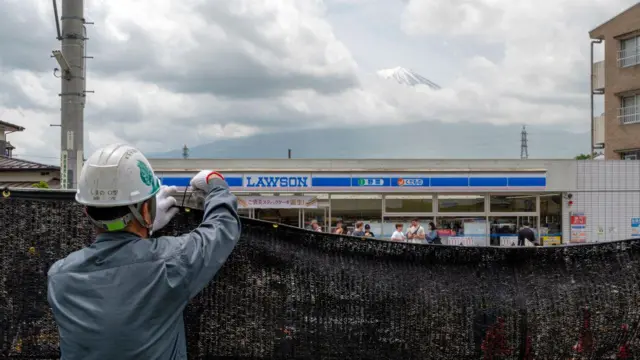 Trabalhador instala uma barreira para bloquear a vista do monte Fuji, no Japão, a fim de deter turistas mal comportados, na cidade de Fujikawaguchiko, no distrito de Yamanashi, em 21 de maio de 2024
