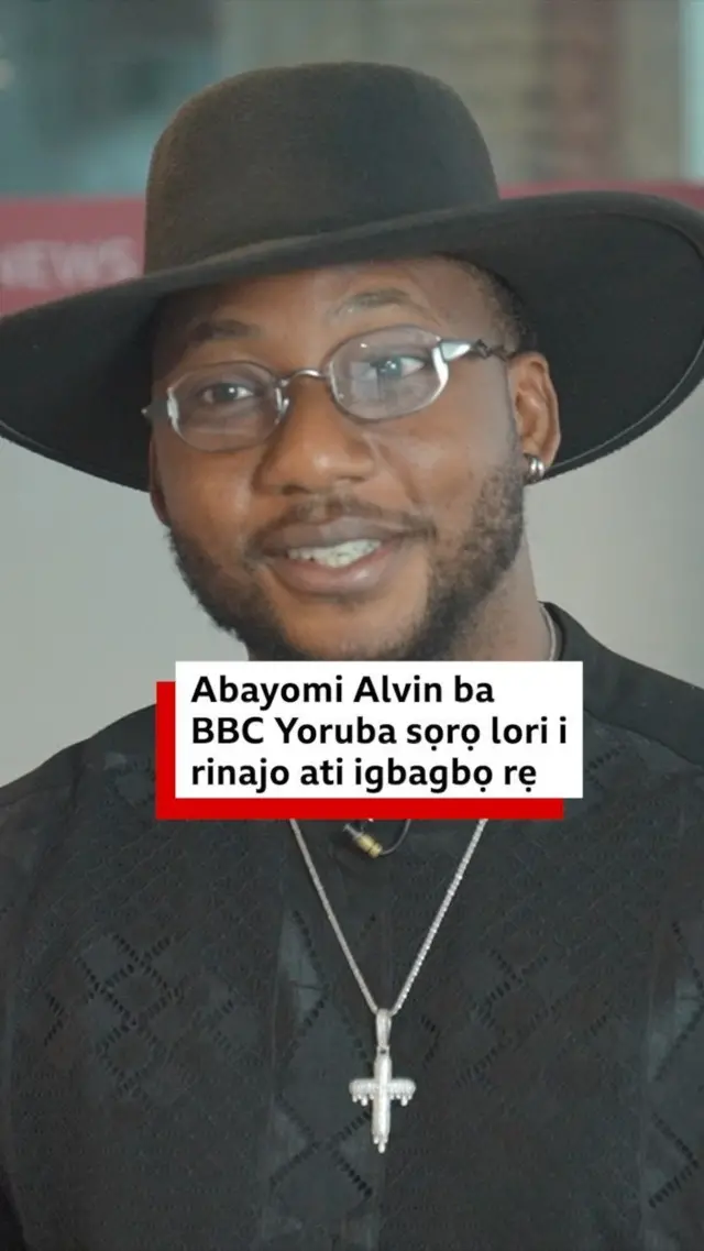 Abayomi Alvin wọ asọ shaati dudu, o de fila bẹnti gọ, o si fi ẹgba ọrun sọrun ati igo soju