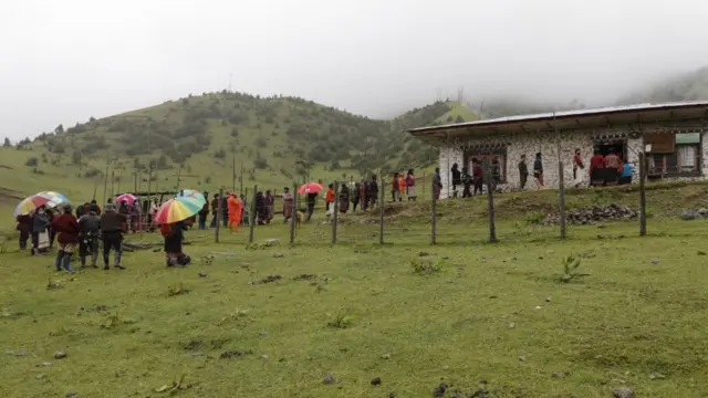 Moradores do vilarejoaposta ganha afiliadoGengu, no distritoaposta ganha afiliadoTrashigang, Butão, fazem fila na chuva do ladoaposta ganha afiliadofora do centro comunitário