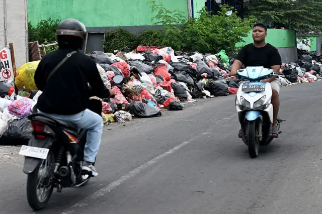 Foto ini diambil pada 21 April 2026 menunjukkan pengendara mobil melewati sampah yang dibuang di sepanjang jalan di Desa Serangan, Denpasar, Bali.
