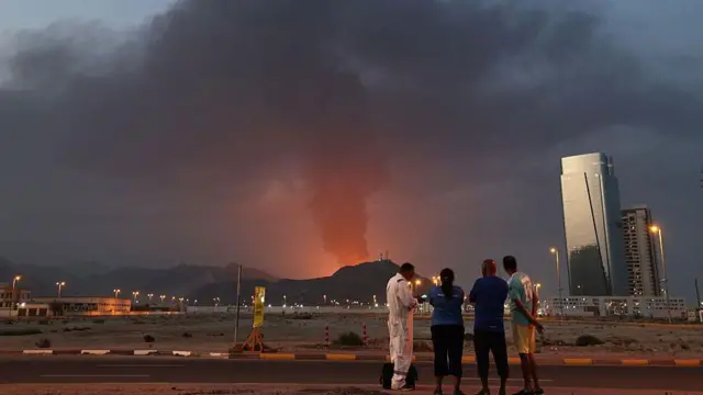 Bir sanayi bölgesinde meydana gelen patlamanın sonrasını izliyen dört kişi görüyoruz. Fotoğrafta bir camekan gökdelen de var.