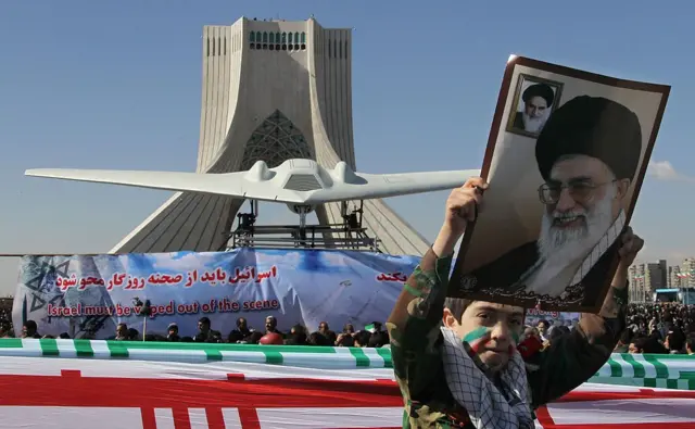 Seorang bocah Iran memegang potret pemimpin tertinggi Ayatollah Ali Khamenei saat dia berjalan melewati replika drone AS RQ-170 yang berhasil dijatuhkan, dan dipamerkan di sebelah Menara Azadi (Kebebasan) pada peringatan ke-33 Revolusi Islam di Teheran, 11 Februari 2012.