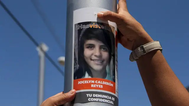 Una manos de mujer colocan un cartel en un poste pidiendo información sobre una mujer desaparecida en Ciudad Juárez