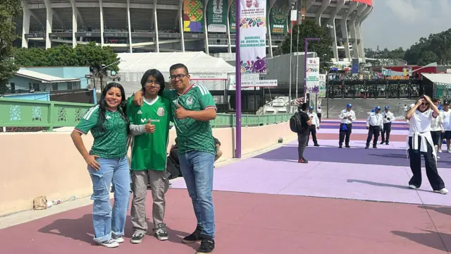 Javier Pérez dan keluarganya, mengenakan jersey Meksiko, berdiri di depan Stadion Azteca sambil memberi isyarat jempol ke arah kamera
