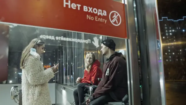 Kirish yoq deb yozilgan oynali bino ichida yoshlar