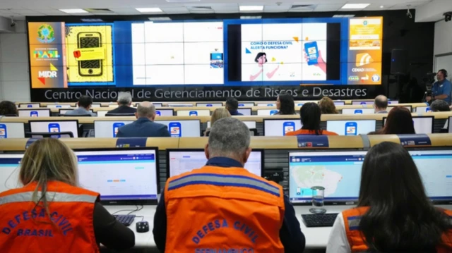 Centro faz envio de alertas por meio de smartphones para todo o país; imagem msotra equipe da Defesa Civil em escritório com computadores