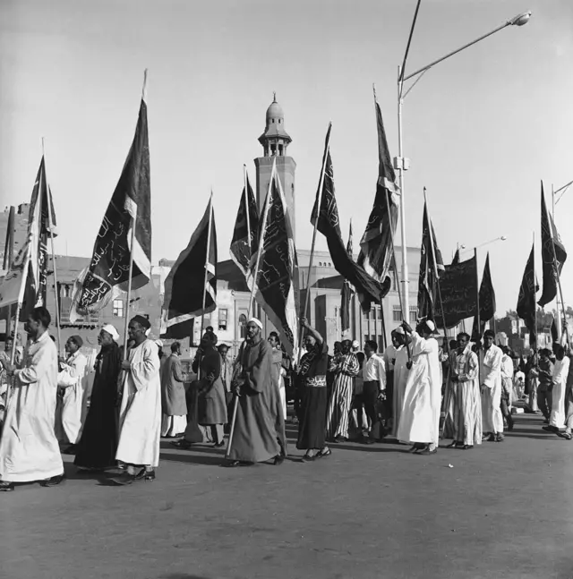 ممثلون عن مختلف الطرق الصوفية يتجهون إلى الجامع الأزهر في القاهرة، بمناسبة ذكرى المولد النبوي الشريف، يحملون راياتهم التي كتبت عليها آيات من القرآن الكريم، 1966.