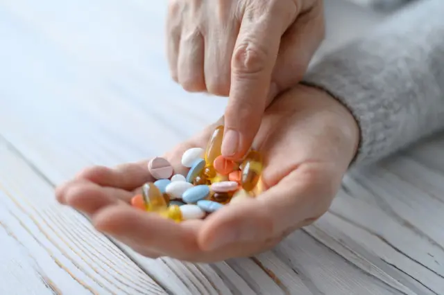Una mujer mira diferentes tipos de pastillas que tiene en la mano