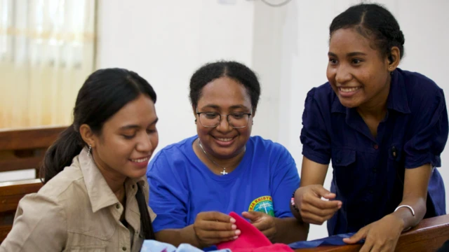 Tiga perempuan sedang membuat kain pembalut.