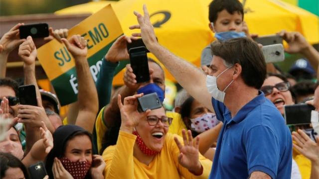 Bolsonaro, de máscara, acena para apoiadores em Brasília