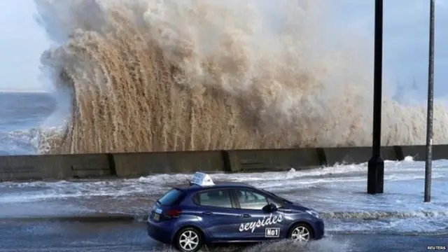 બ્રિટનના મર્સીસાઇડ વિસ્તારમાં પૂરના પાણીથી ભરાયેલાં રસ્તા પર પસાર થતી કાર.