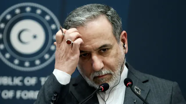 Мужчина с седой бородкой и усами и темными волосами с проседью задумчиво поднес ко лбу руку. На пальце у него кольцо с темно-красным камнем