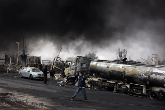 Radnici posmatraju dim koji se i dalje diže iz rafinerije nafte Šahran posle vazdušnog napada na Teheranu, Iran, 8. marta 2026. 