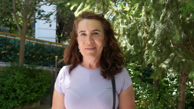 Hacer Bulut'un BBC Türkçe'ye verdiği röportajdan fotoğrafı. Üzerinde mor tişört, kafasında güneş gözlüğü ve kolunda el çantası var.