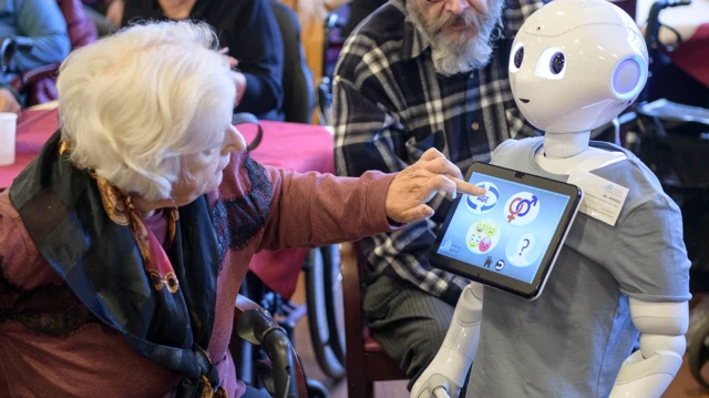 一位老妇人看着机器人，触摸其正面的萤幕