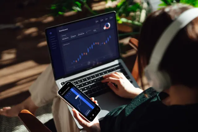 Una persona mirando sus finanzas en su computador y su teléfono.