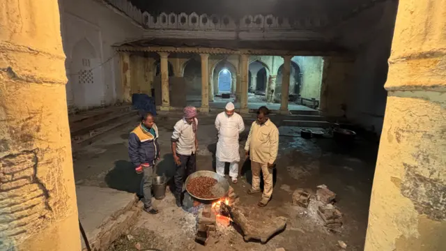 Four men stand around a big plate of kebabs which are being cooked on a traditional wood fired stove at the Shahi Bawarchikhana inside Chota Imambara in Lucknow.