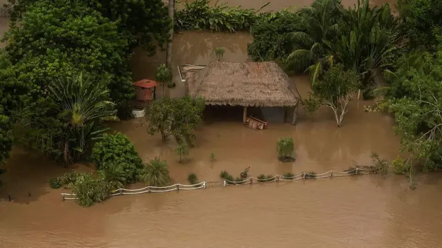 Imagen aérea muestra una cabaña rural con techo de paja en medio de una parcela inundada