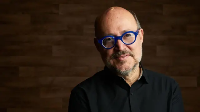 Una foto de Ricardo Raphael, escritor y periodista mexicano, con gafas de montura azul y gesto sonriente