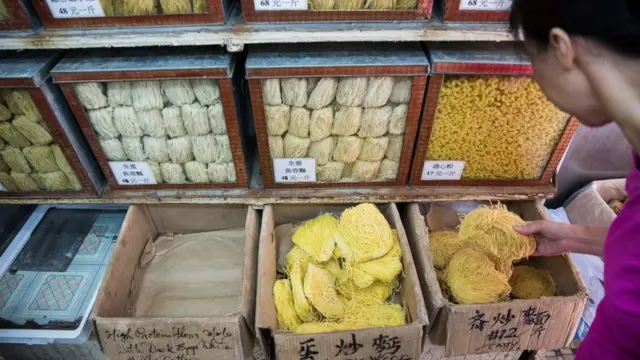 Mujer comprando noodles en un mercado de Hong Kong