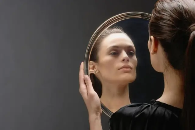 Mulher branca jovem olha para seu reflexo em um espelho