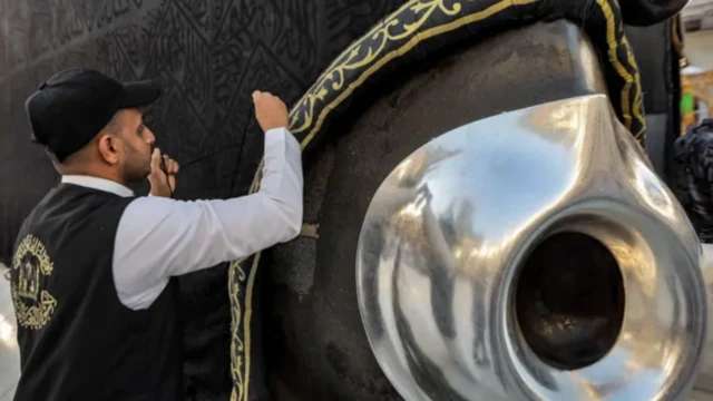 Ọkunrin kan to wọ aṣọ dudu ati funfun duro sẹgbẹẹ okuta dudu ni Kaaba