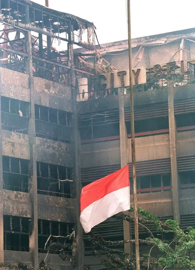 Bendera Indonesia berkibar setengah tiang 16 Mei di depan sisa-sisa hotel yang membara dan terbakar di daerah pecinan Jakarta.