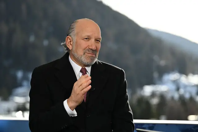 Howard Lutnick colocando uma das mãos sobre a gravata. Ele usa um terno preto. 