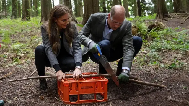 Kate e William agachadoshistórico roleta brasileirameio à floresta; ele corta pedaçohistórico roleta brasileiralenha, e ela ajuda